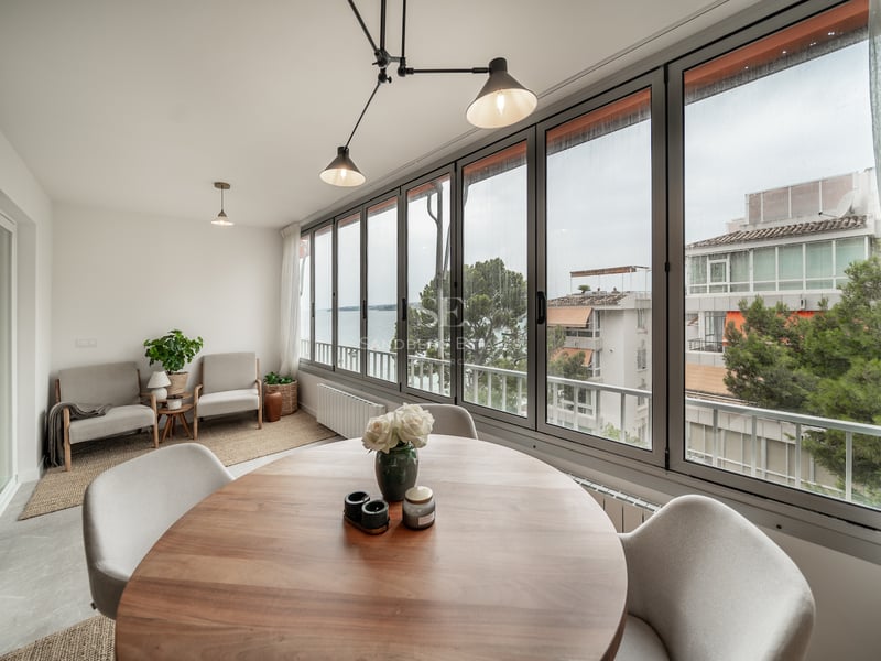 Salle à manger moderne avec table ronde en bois, grandes baies vitrées et vue sur la côte méditerranéenne.