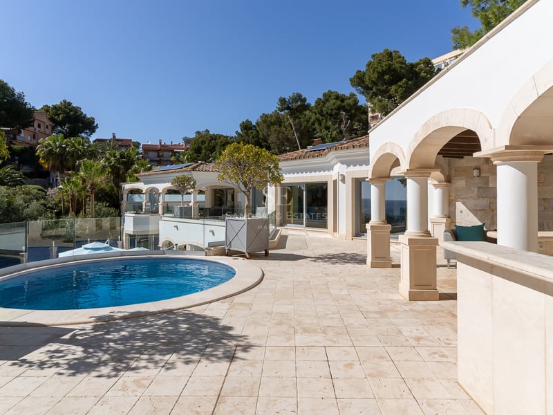 Terrasse de luxe avec sol en pierre, colonnes cintrées et piscine circulaire bleue par temps clair.