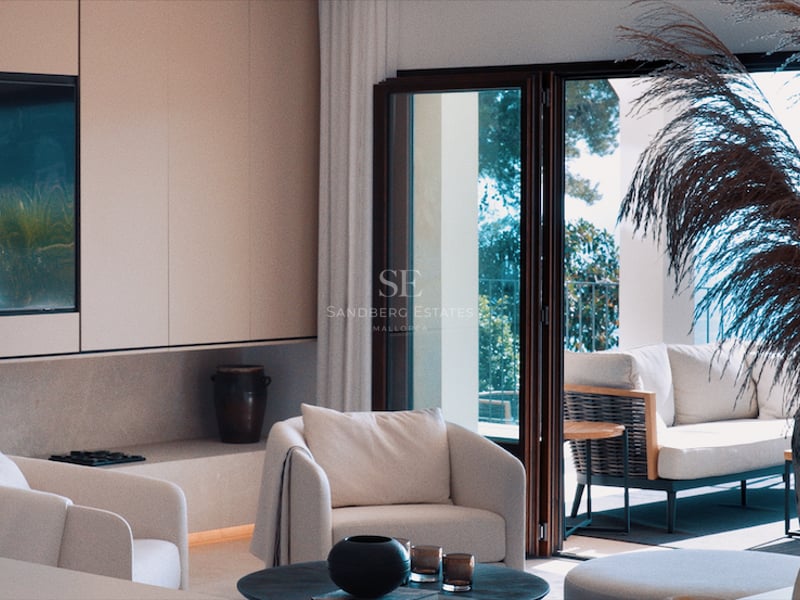 Salon minimaliste lumineux avec fauteuils blancs, grand téléviseur intégré et baies vitrées ouvrant sur une terrasse.