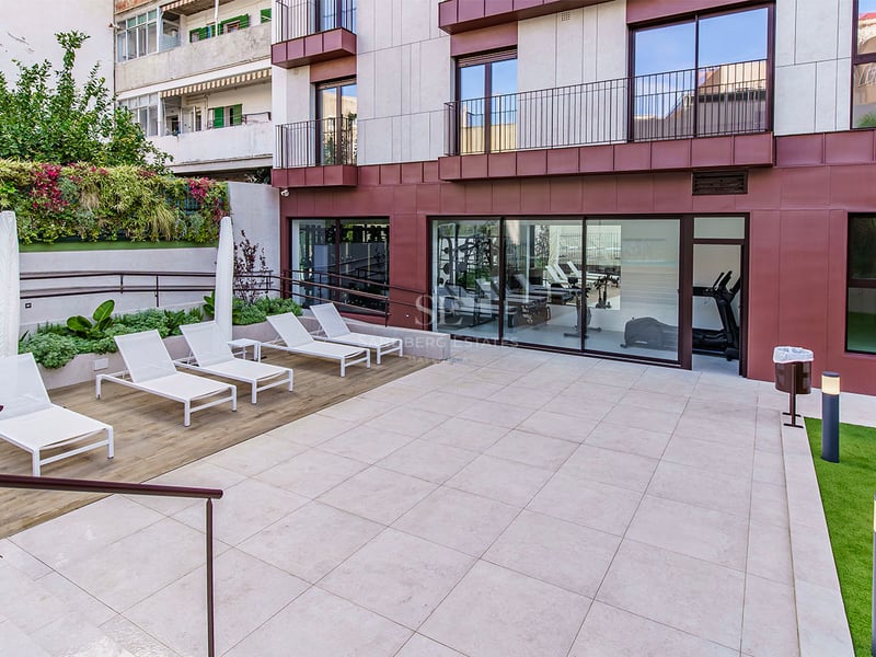 Terrasse extérieure moderne avec transats blancs, jardin vertical et vue sur une salle de sport vitrée.