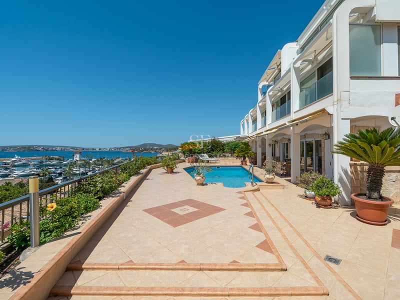 Grande terrasse extérieure avec piscine et vue sur un port de plaisance sous un ciel bleu.