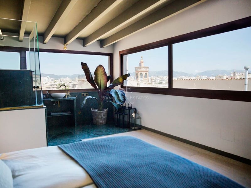 Dormitorio moderno con vigas de madera vistas, ventanales panorámicos y vistas a la catedral y la ciudad.