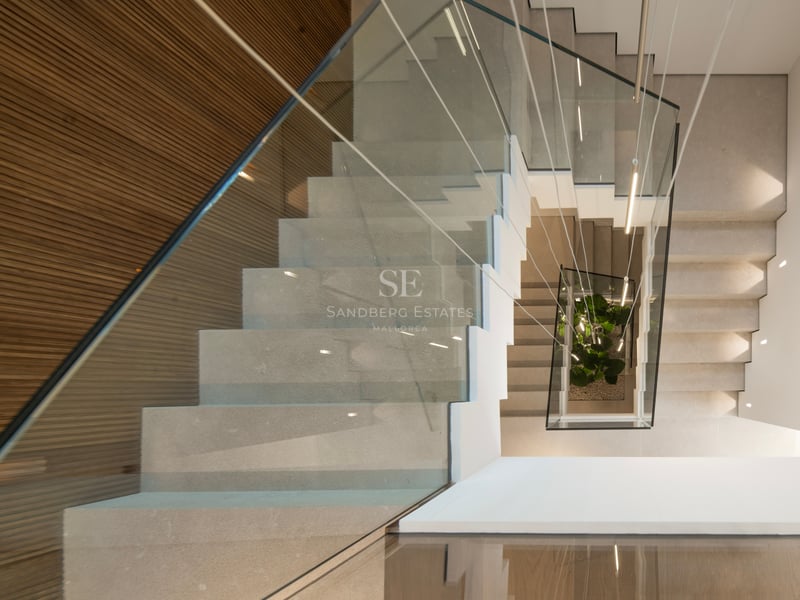 Vue de dessus d'un escalier moderne en pierre avec garde-corps en verre, mur en bois et luminaires suspendus.