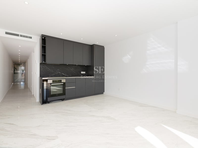 Espace cuisine moderne avec armoires gris foncé, crédence en marbre noir et sols en marbre blanc dans une pièce lumineuse.