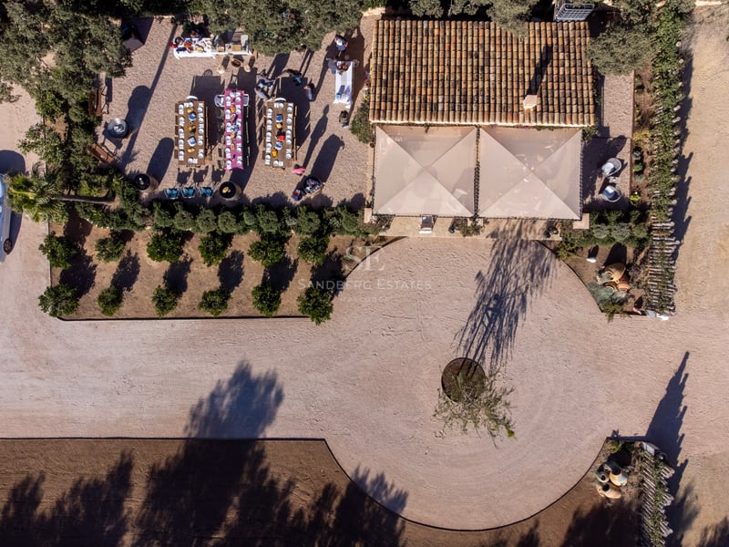 Vue plongeante d'une villa de luxe montrant les toits de tuiles, un espace repas extérieur et une allée circulaire.