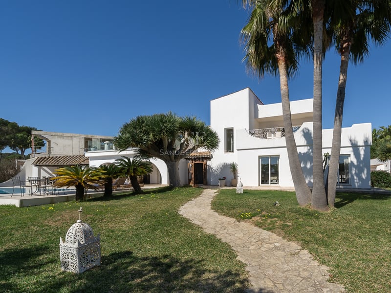 Villa méditerranéenne blanche avec un chemin en pierre, des palmiers et une piscine sous un ciel bleu éclatant.