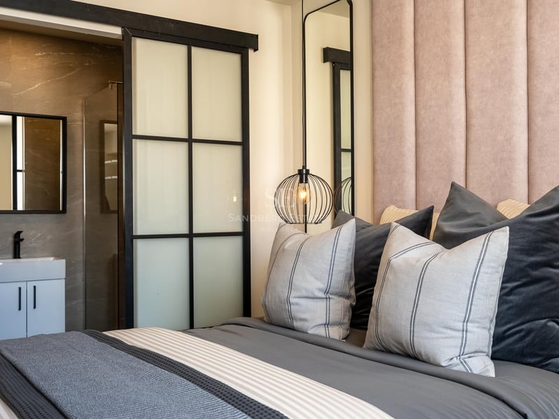 Chambre avec tête de lit en velours rose, luminaire design et porte coulissante industrielle menant à la salle de bain.