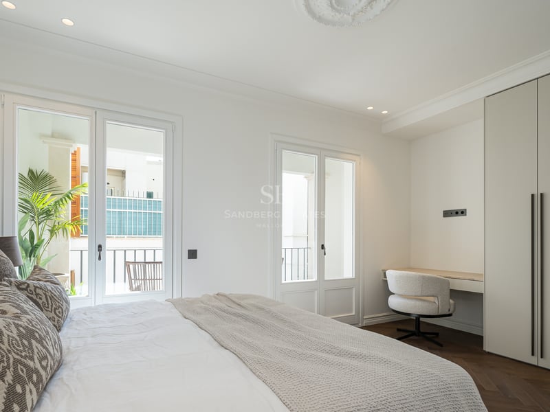 Spacious master bedroom featuring herringbone wood floors, built-in wardrobes, a desk, and French doors to a balcony.