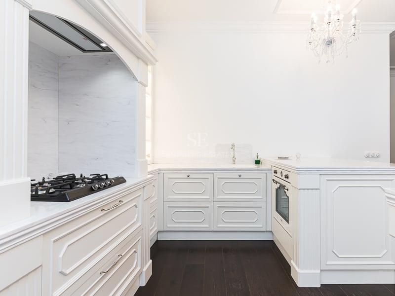 Cuisine blanche élégante avec plans de travail en marbre, parquet sombre et lustre en cristal.