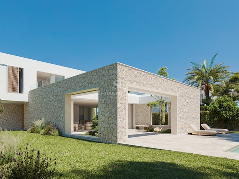 Extérieur d'une villa contemporaine avec murs en pierre naturelle, grandes baies vitrées et pelouse sous un ciel bleu.