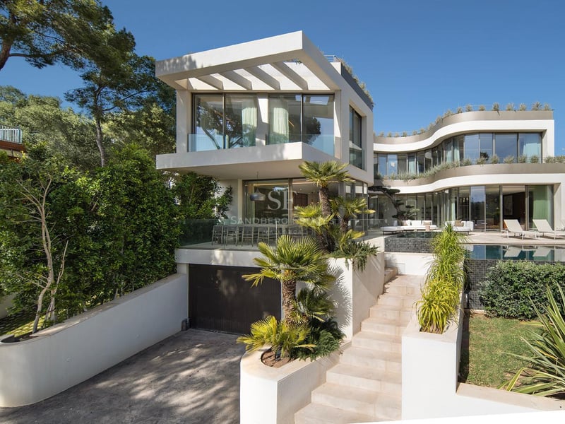 Villa moderne blanche à plusieurs niveaux avec façades vitrées courbes, piscine, palmiers et escalier en pierre.