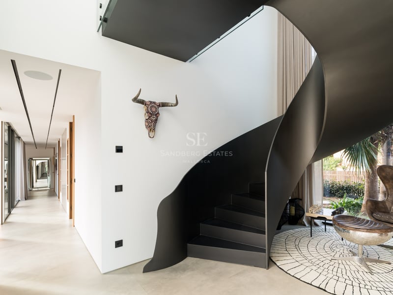 Escalier en colimaçon moderne en métal noir mat dans une villa lumineuse aux murs blancs.