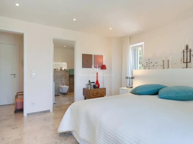 Chambre moderne avec literie blanche, coussins turquoise, sol en marbre et vue sur la salle de bains en pierre.
