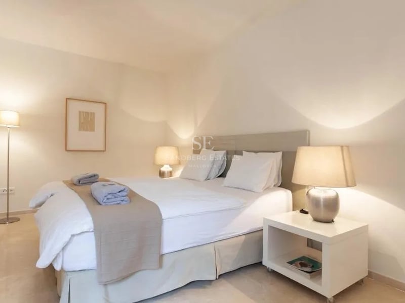 Chambre moderne avec lit double, draps blancs, lampes de chevet et sol en pierre naturelle.