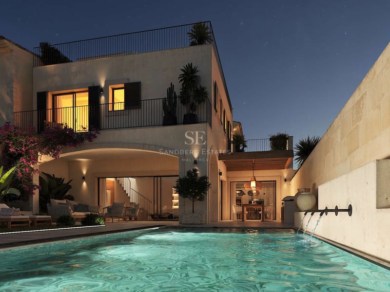 Vue nocturne d'une villa de luxe avec piscine éclairée, jets d'eau, murs en pierre et ciel étoilé.
