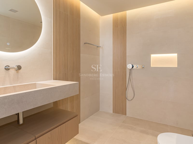 Modern bathroom featuring a circular backlit mirror, integrated stone vanity, and vertical wood slat wall detailing.