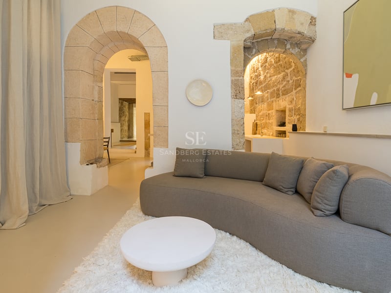 Un salon moderne avec un canapé gris incurvé, un tapis blanc et de grandes arches en pierre historiques.