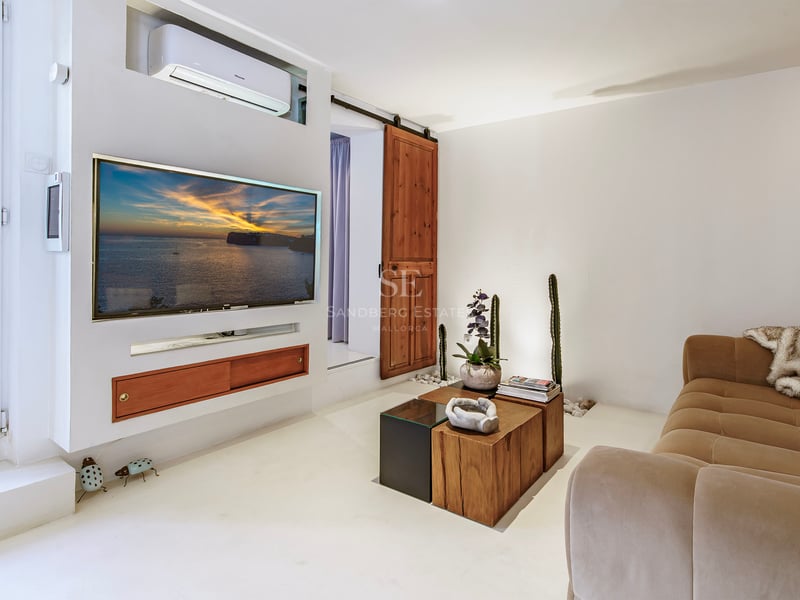 Salon blanc chaleureux avec télévision murale, grand canapé beige et porte de grange coulissante en bois.