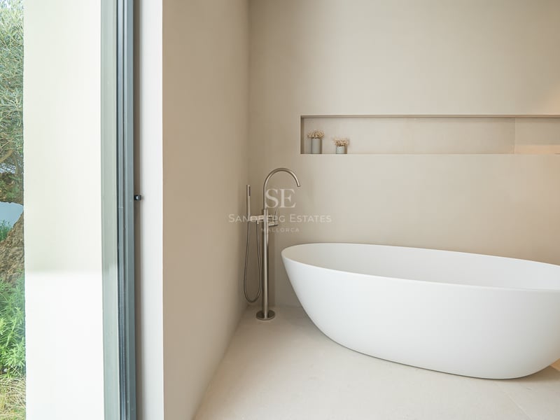 Salle de bain moderne avec baignoire îlot blanche et grande baie vitrée donnant sur un olivier.