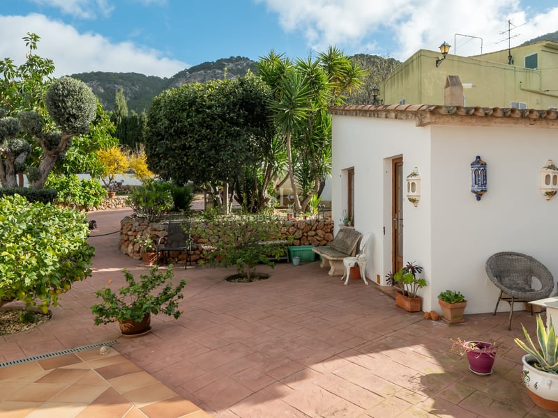 Patio en terre cuite avec annexe blanche, végétation luxuriante et vue sur les montagnes environnantes.