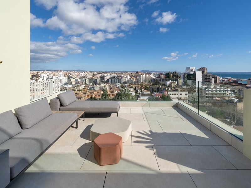 Toit-terrasse moderne avec canapés gris et garde-corps en verre offrant une vue sur la ville et la mer.