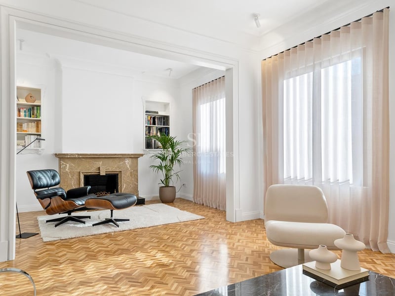 Salon lumineux avec parquet en chevrons, cheminée en marbre et fauteuil Eames.