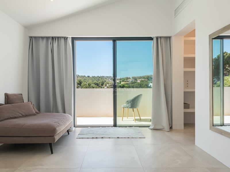 Chambre moderne avec baies vitrées ouvrant sur une terrasse ensoleillée avec vue sur la nature.
