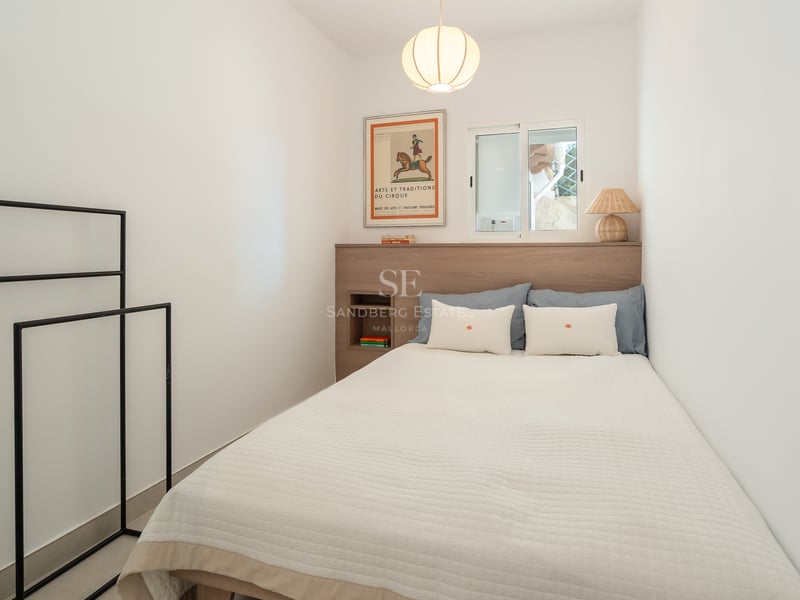 Une chambre minimaliste avec un lit blanc, une tête de lit en bois clair, une fenêtre et une suspension en papier.