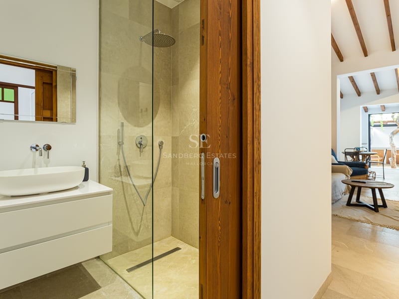 Salle de bain contemporaine avec douche en pierre, meuble vasque blanc et porte coulissante en bois.