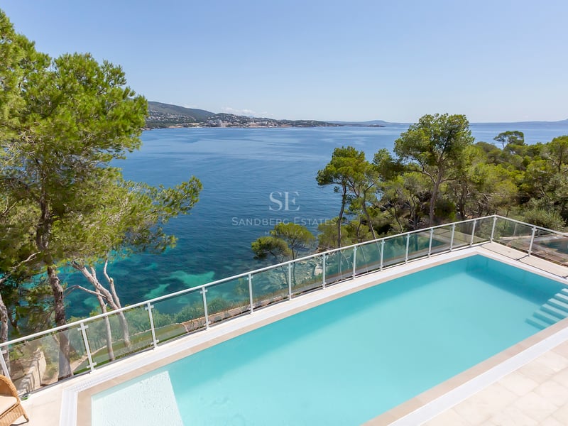 Piscine rectangulaire turquoise surplombant la mer Méditerranée avec des pins et un garde-corps en verre.
