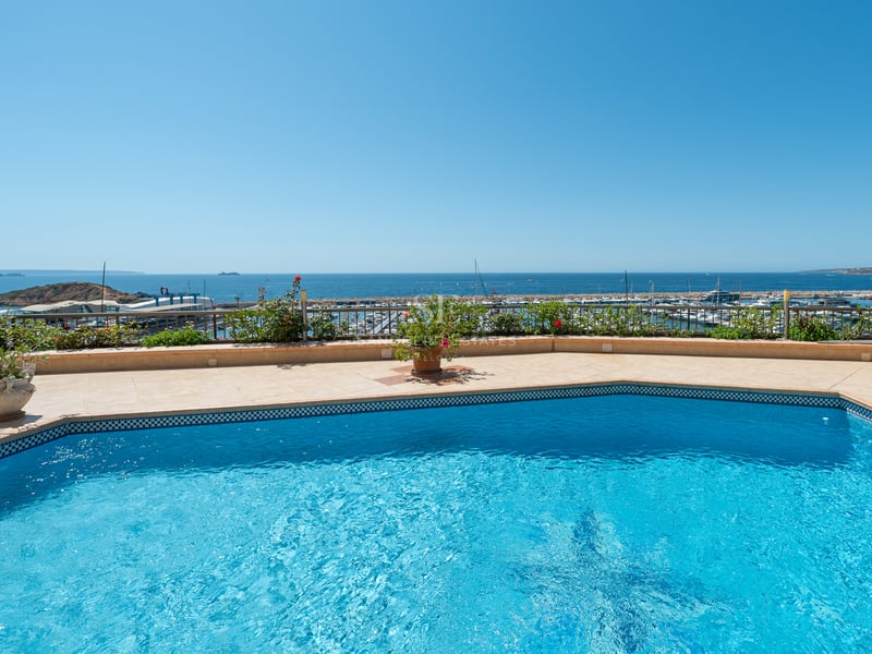 Terrasse avec piscine en mosaïque bleue et vue sur un port de plaisance méditerranéen sous un ciel bleu.