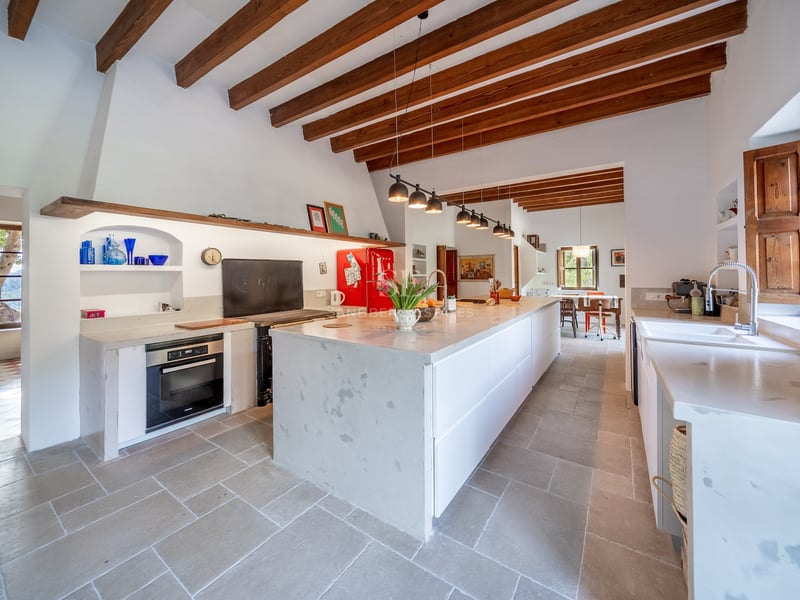 Cuisine spacieuse avec poutres en bois apparentes, grand îlot en pierre blanche et réfrigérateur rouge rétro.