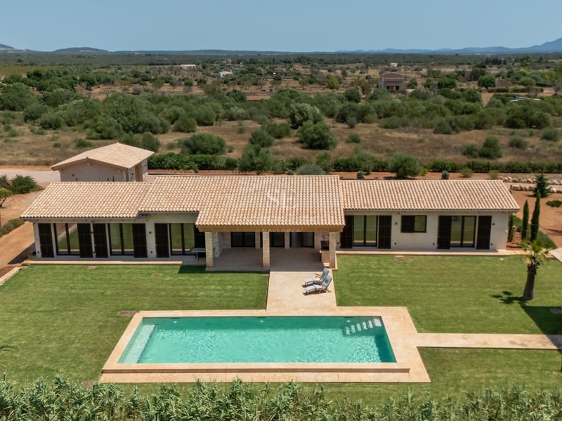 Vista aérea de una villa de lujo con piscina rectangular, césped cuidado y tejado de tejas árabes.