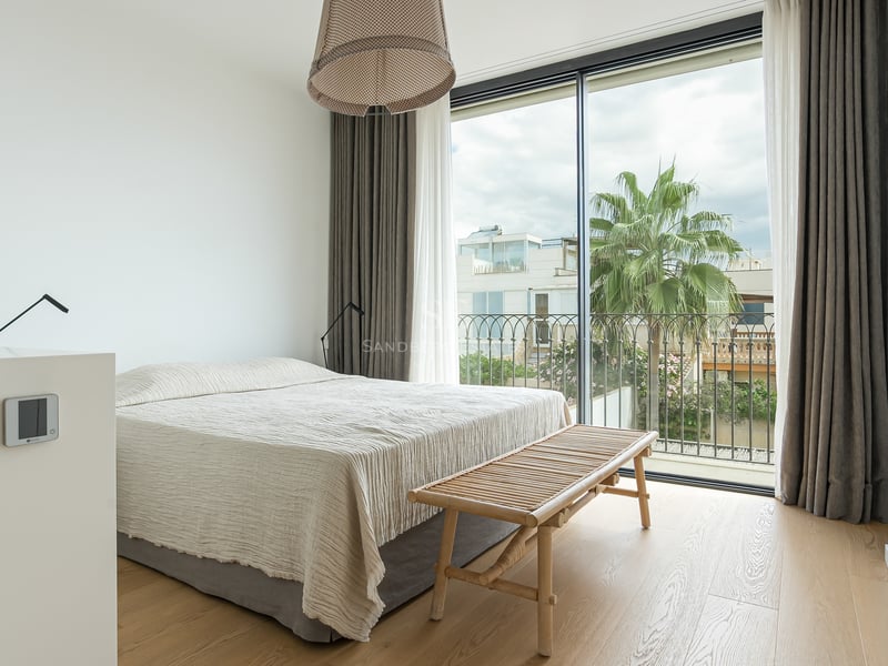 Chambre lumineuse avec baies vitrées, parquet en bois clair, grand lit et vue sur un palmier à l'extérieur.