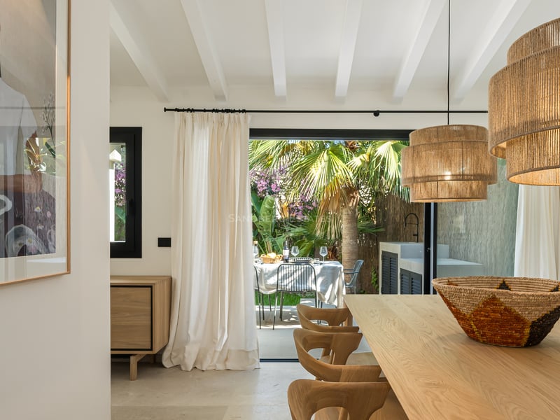 Salle à manger moderne avec table en chêne et suspensions en jute, s'ouvrant sur une terrasse de jardin luxuriante.