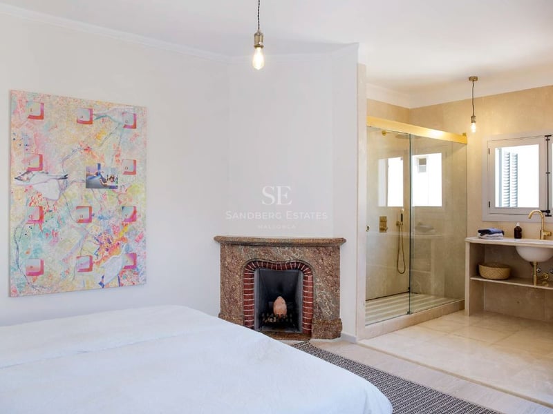 Amplio dormitorio principal con chimenea decorativa, arte moderno y baño integrado con paredes de cristal.