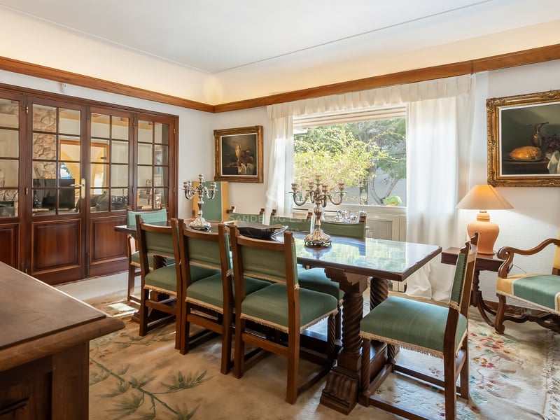 Salle à manger traditionnelle avec table en bois foncé, chaises vertes, candélabres en argent et tableaux classiques.