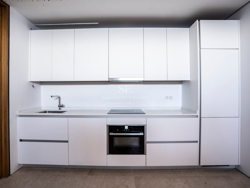Cuisine blanche moderne avec placards sans poignées, four encastré, plaque à induction et évier en inox.