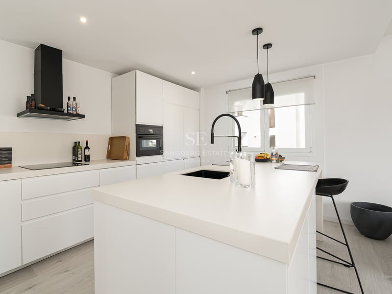 Cuisine blanche moderne avec un grand îlot, un robinet noir et des appareils électroménagers intégrés.