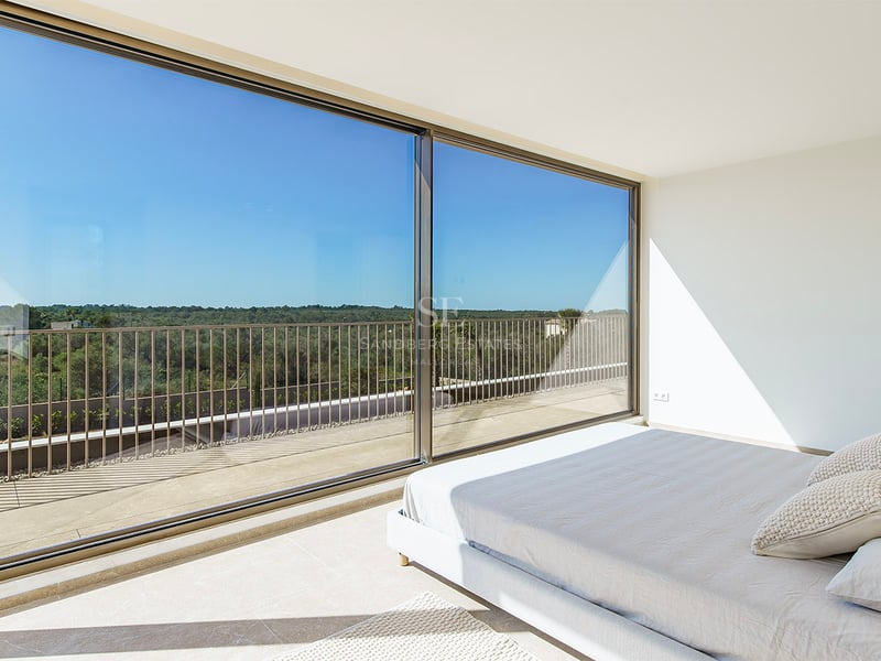 Chambre principale lumineuse avec de grandes baies vitrées coulissantes ouvrant sur une terrasse surplombant la nature.
