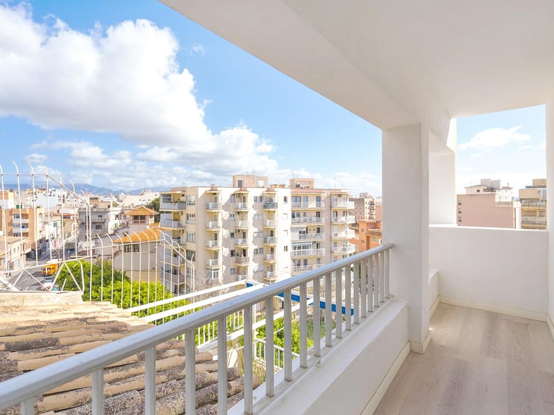 Balcon blanc lumineux avec sol en bois clair surplombant des immeubles urbains et des montagnes au loin.