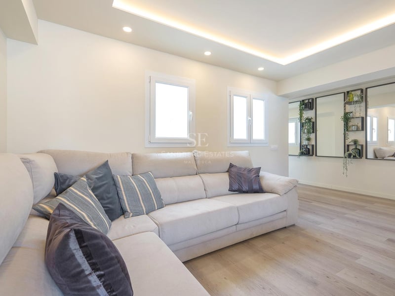 Salon moderne avec un grand canapé en L crème, parquet clair et éclairage au plafond encastré.