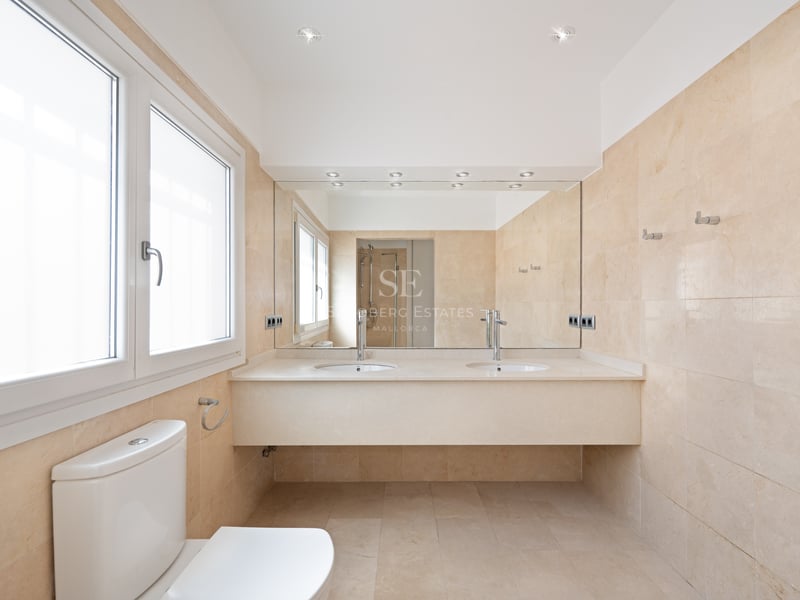 Salle de bains contemporaine avec murs en marbre crème, double vasque, grand miroir et fenêtre lumineuse.
