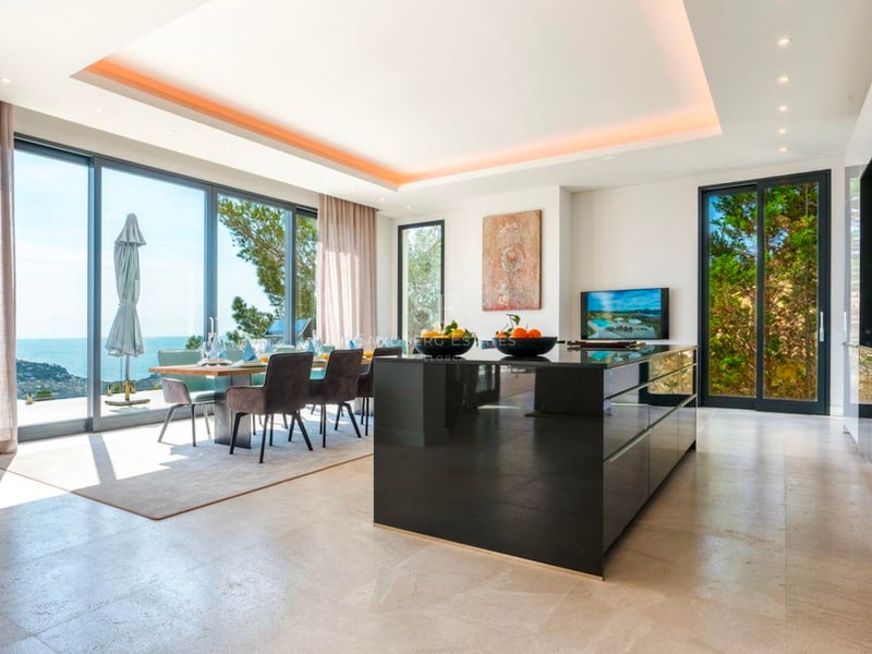 Cuisine et salle à manger modernes avec îlot noir brillant et grandes fenêtres offrant une vue sur la mer.