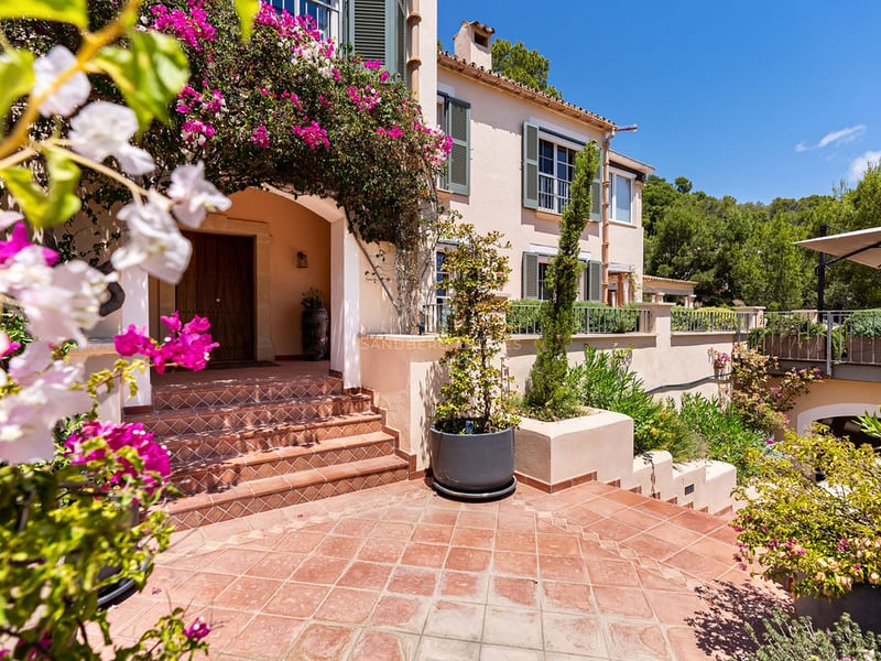 Marches en terre cuite menant à une porte en bois d'une villa encadrée de bougainvilliers roses.