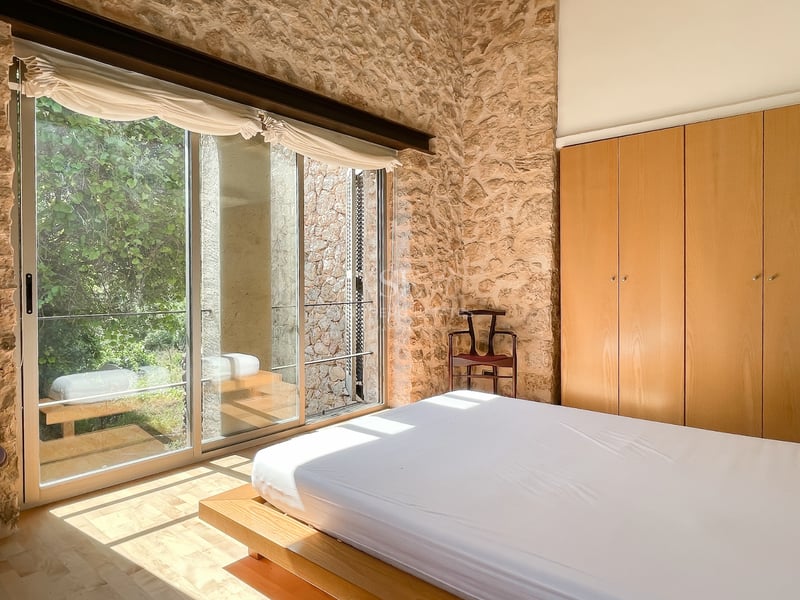 Chambre avec murs en pierre apparente, grandes baies vitrées coulissantes et placards intégrés en bois.