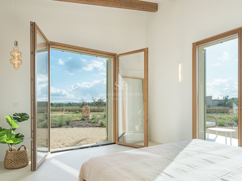 Bright bedroom featuring large wood-framed glass doors opening onto a Mediterranean landscape with olive trees.