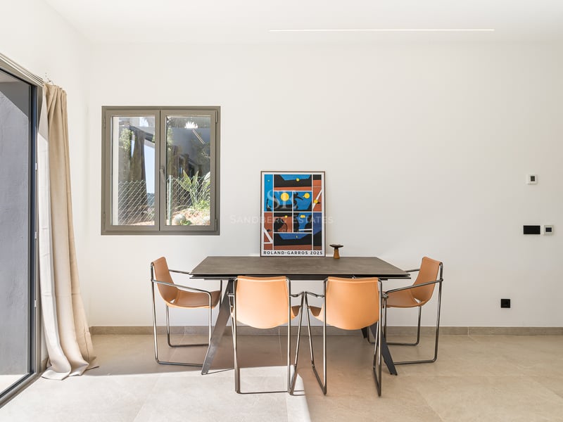 Salle à manger moderne avec table en pierre, chaises en cuir fauve et grandes baies vitrées coulissantes.