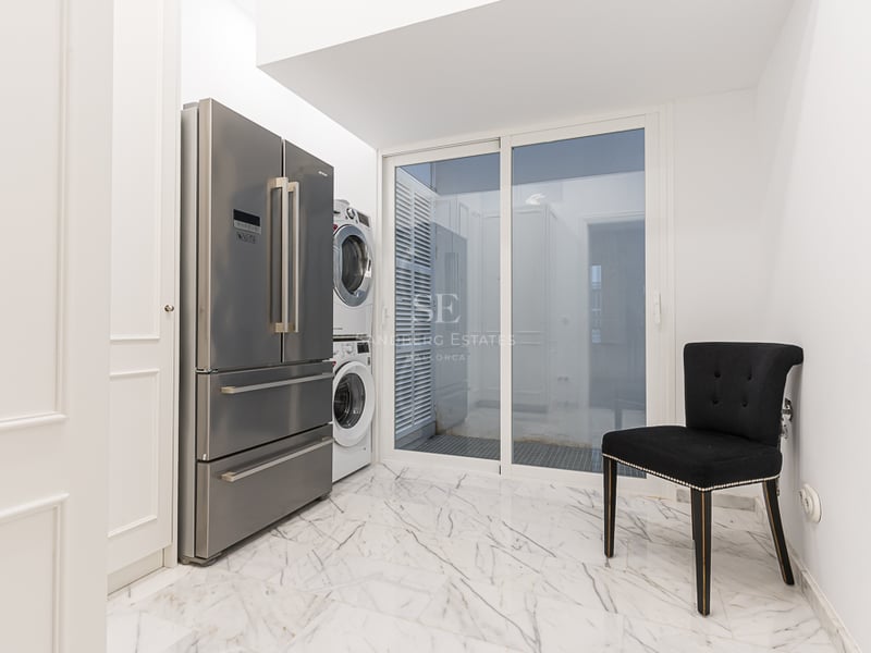 Buanderie avec réfrigérateur en inox, lave-linge et sèche-linge superposés, et sol en marbre blanc.
