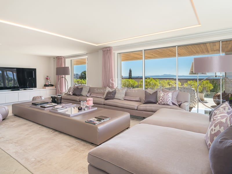 Salon spacieux avec canapé taupe et grandes baies vitrées offrant une vue sur le jardin et la mer.
